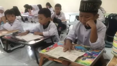 Kabupaten Bekasi - Murid dari 4 kelas yang ada di SDN Sukadanau 04, di Kecamatan Cikarang Barat, Kabupaten Bekasi terpaksa harus belajar di lantai dengan meja lipat yang dibawa sendiri dari rumah, lantaran disekolah tersebut belum ada fasilitas meja dan kursi. Foto: Beritasatu