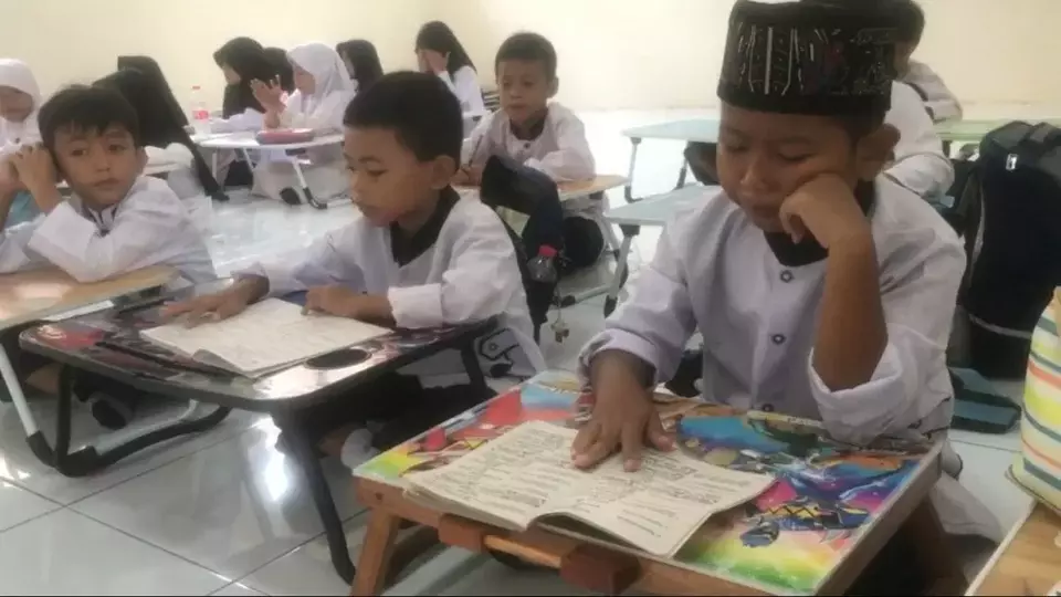 Kabupaten Bekasi - Murid dari 4 kelas yang ada di SDN Sukadanau 04, di Kecamatan Cikarang Barat, Kabupaten Bekasi terpaksa harus belajar di lantai dengan meja lipat yang dibawa sendiri dari rumah, lantaran disekolah tersebut belum ada fasilitas meja dan kursi. Foto: Beritasatu