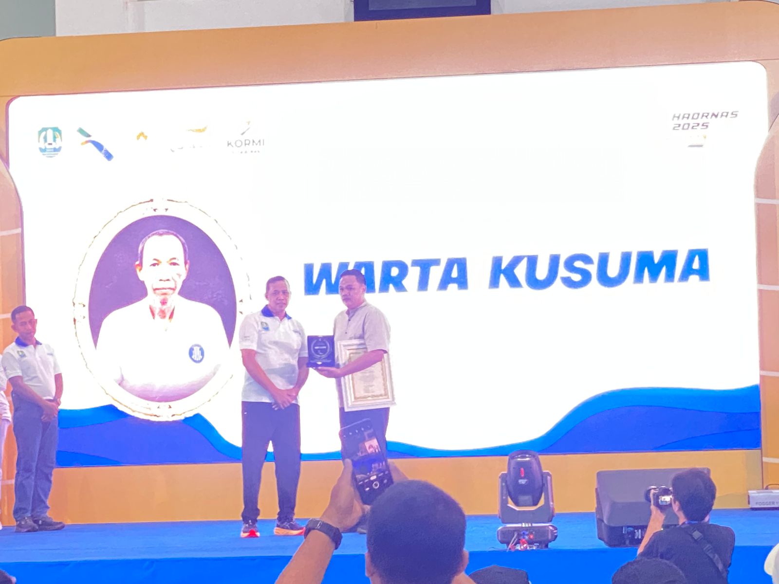 Kota Bekasi - Wali Kota Bekasi Tri Adhianto memberikan apresiasi terhadap Almarhum Warta Kusuma yang diwakili oleh putranya dalam puncak peringatan Haornas di Kota Bekasi, Sabtu (27/9/2025). Foto: Gobekasi.id.